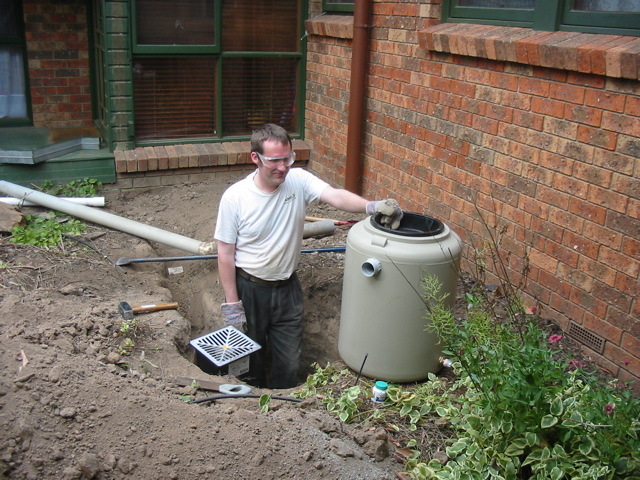 Grant building his downspout water diverter. It is pumped from this little tank under the house to ---->